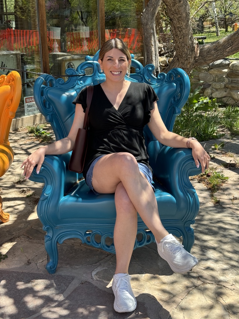 Ashley sitting in a poly chair wearing an Ekouaer Maternity Shirt from Amazon